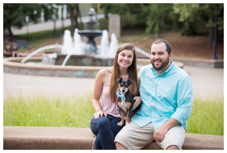 man and a woman sitting in front of a fountain with a dog